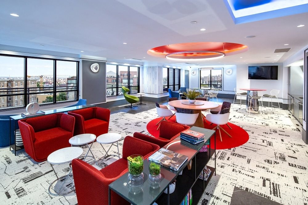 a lounge area with red chairs and tables and a large window